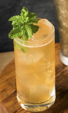 a tall glass filled with ice and mint sitting on top of a wooden table next to a metal cup