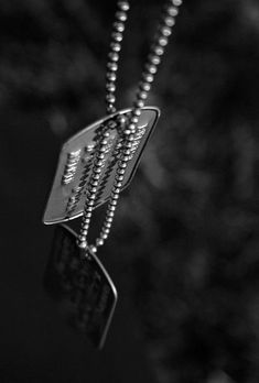 a black and white photo of a dog tag on a beaded necklace with the word love written across it