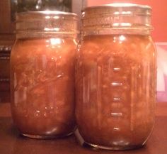 two jars filled with brown liquid sitting on top of a wooden table next to a clock