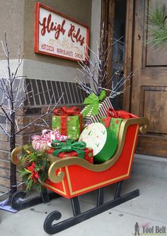 a sleigh filled with presents sitting on the side of a building next to a tree