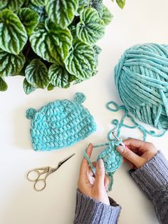 someone is crocheting the yarn for a hat with scissors and a plant in the background