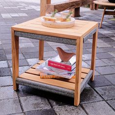 a wooden table sitting on top of a sidewalk next to a basket filled with books