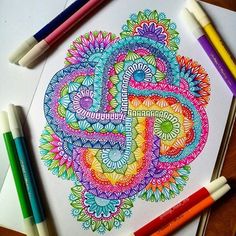 a coloring book with colored pencils and markers on the table next to some pens