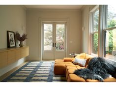 a living room with an orange couch and two large windows on the side of it