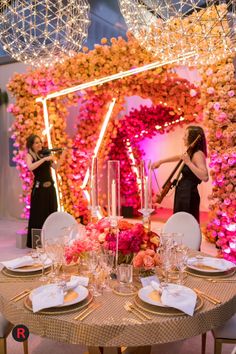 a table set up with plates and place settings for two women in front of a floral archway