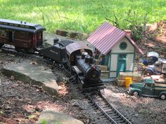 a toy train traveling through a forest next to a small house and car on the tracks