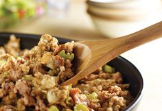 a pan filled with rice and vegetables on top of a table next to a wooden spoon