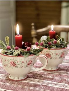 two coffee cups with holly and berries on them, one has a lit candle in the middle