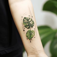 a green leaf tattoo on the left forearm and right arm, with black dots around it