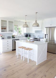 a white kitchen with two stools in front of the island and an open floor plan