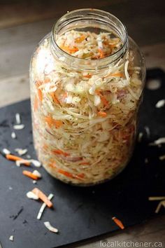 a glass jar filled with coleslaw on top of a black cutting board next to carrots