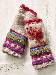 two knitted mittens sitting on top of a white wooden floor next to each other