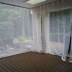 an empty room with sheer curtains on the windows and wood flooring in front of it