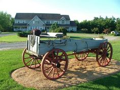 an old fashioned horse drawn carriage sitting in front of a large white house with red trim