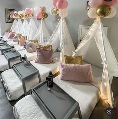 a room filled with lots of white beds covered in pink and gold pillows next to balloons