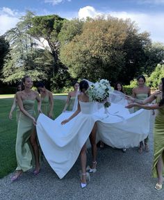 a group of bridesmaids in green dresses are pulling the bride's dress