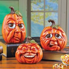 three pumpkins with faces carved into them sitting on top of a table next to some candy