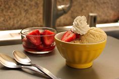 a bowl of ice cream with strawberries in it and two spoons on the side