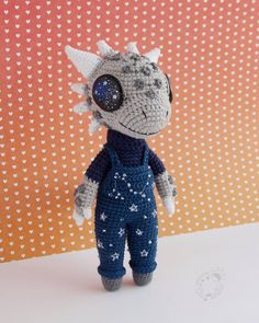 a crocheted stuffed animal wearing overalls and eyeglasses with hearts in the background