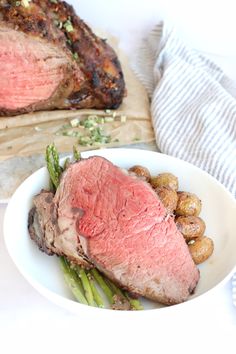 a white plate topped with meat and potatoes next to a piece of meat on top of asparagus