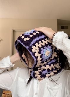 a woman wearing a crocheted hat and scarf in the kitchen with her hands on her head