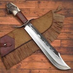 a large knife is sitting on top of a piece of leather and has fringed handles