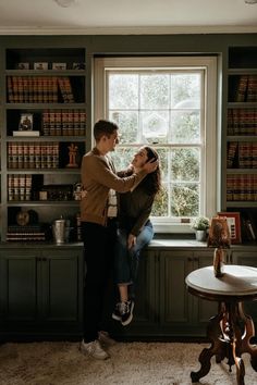 a man helping a woman put on her hair in front of a window with bookshelves