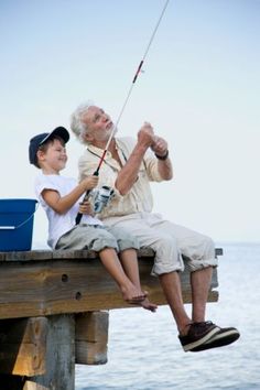 an older man and young boy sitting on a dock fishing