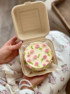 a woman is holding a cake in a plastic box with pink roses on the frosting