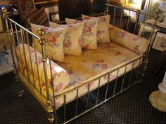 a gold metal day bed with four pillows on it's sides and some framed pictures in the background