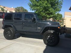 a gray jeep parked in a parking lot next to a tree and building on a sunny day