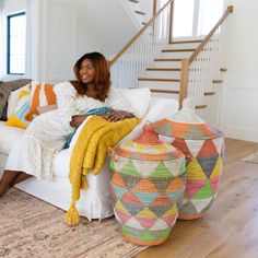 a woman sitting on a white couch next to two colorful baskets and a stair case