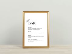 a bar menu is displayed in a gold frame on a table with a white wall behind it