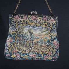 A ladies handbag with gold coloured metal clasp with dots. Vintage handmade. Fine example of a cosy lady's handbag of the beginning of the last century. Embroidered fabric with a landscape surrounded by flowers on both sides of the bag. Ivory coloured satin inside. Lovingly made. Vintage. Size  W 16 H 16 cm. It has been around for a long time but just a tiny bit of wear. Still beautiful and surely wearable on your next garden party. Please have a look at all our vintage handbags in the  - Ladies Vintage Tapestry Pouch Bag, Vintage Handmade Tapestry Bag, Vintage Tapestry Handmade Bags, Vintage Embroidered Rectangular Evening Bag, Vintage Embroidered Tapestry Shoulder Bag, Antique Tapestry Bags For Everyday, Victorian Style Embroidered Rectangular Bag, Antique Handmade Rectangular Shoulder Bag, Victorian Style Rectangular Tapestry Bag