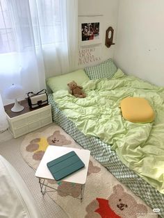 a bed with green sheets and a teddy bear on it in a bedroom next to a window