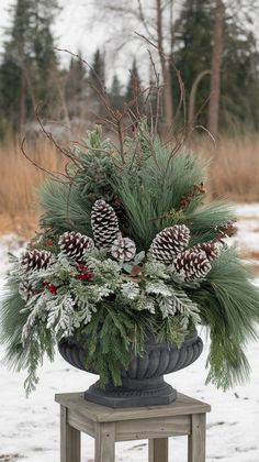 a vase filled with pine cones and evergreens on top of a wooden table in the snow