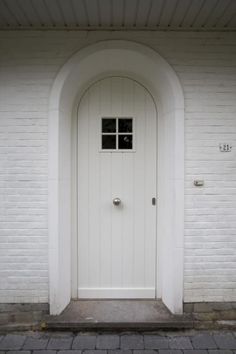 a white door is in front of a brick building with an arched doorway and two windows