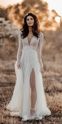 a woman wearing a long white dress standing in the middle of a dry grass field