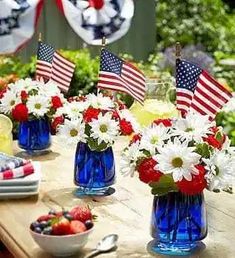 red, white and blue flowers are in vases on a picnic table with strawberries