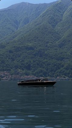 a boat floating on top of a large body of water next to a lush green mountain