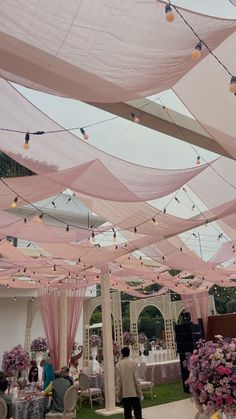 an outdoor wedding with pink draping and floral centerpieces on the ceiling