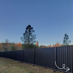 a long black fence with an arrow drawn on it's side in front of some trees