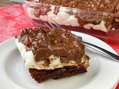 a piece of cake on a plate with a fork next to it and a glass dish full of desserts in the background