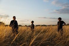 three people standing in the middle of a tall grass field at sunset with one person throwing a frisbee