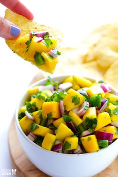 a white bowl filled with fruit and veggies next to potato chips on a cutting board