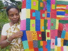 a woman holding up a colorful quilt in front of her face and smiling at the camera