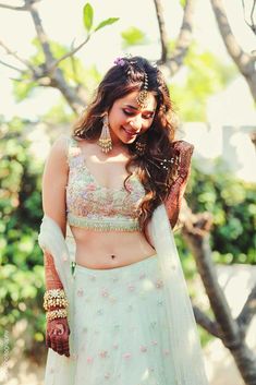 a woman in a white and pink lehenga standing next to a tree with her hands on her hips