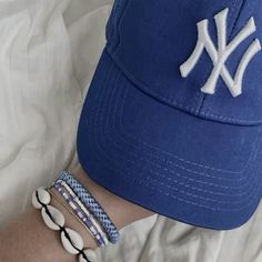 a person wearing a new york yankees hat and three bracelets on their arm, while laying in bed