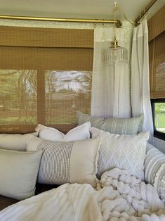 a bed with pillows and blankets on it in front of a window that has blind shades