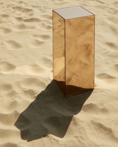 a mirrored object sitting in the sand on top of a sandy beach at day time